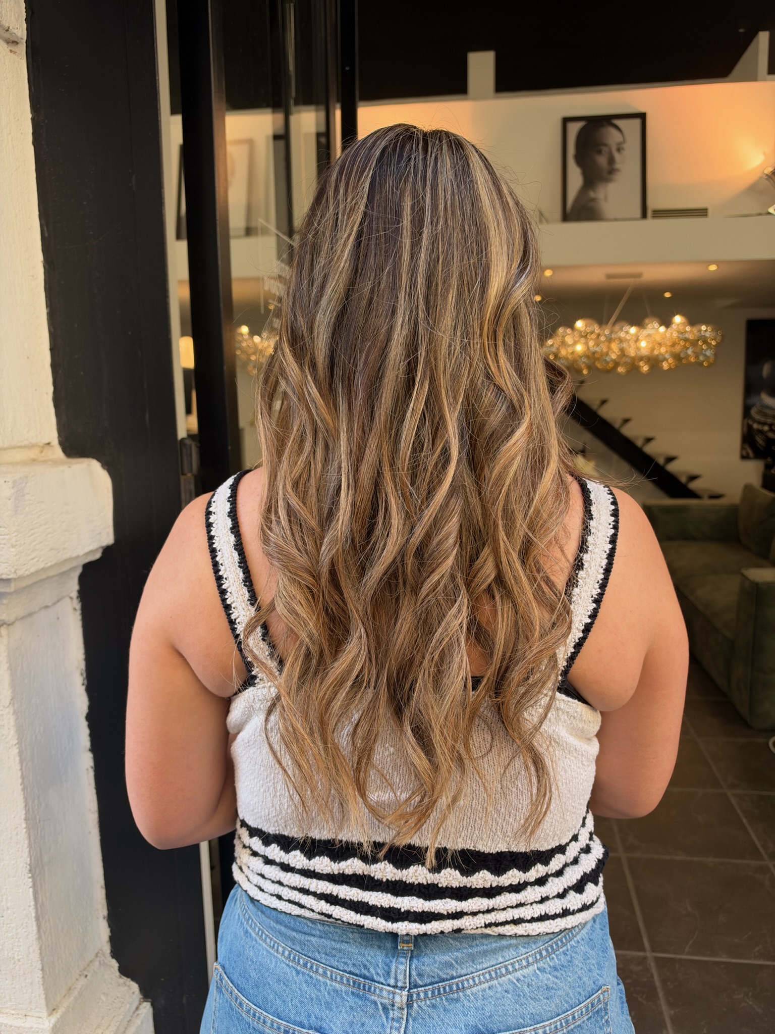 Vue de dos de cheveux longs ondulés, balayage blond miel, caramel et doré sur base châtain naturel