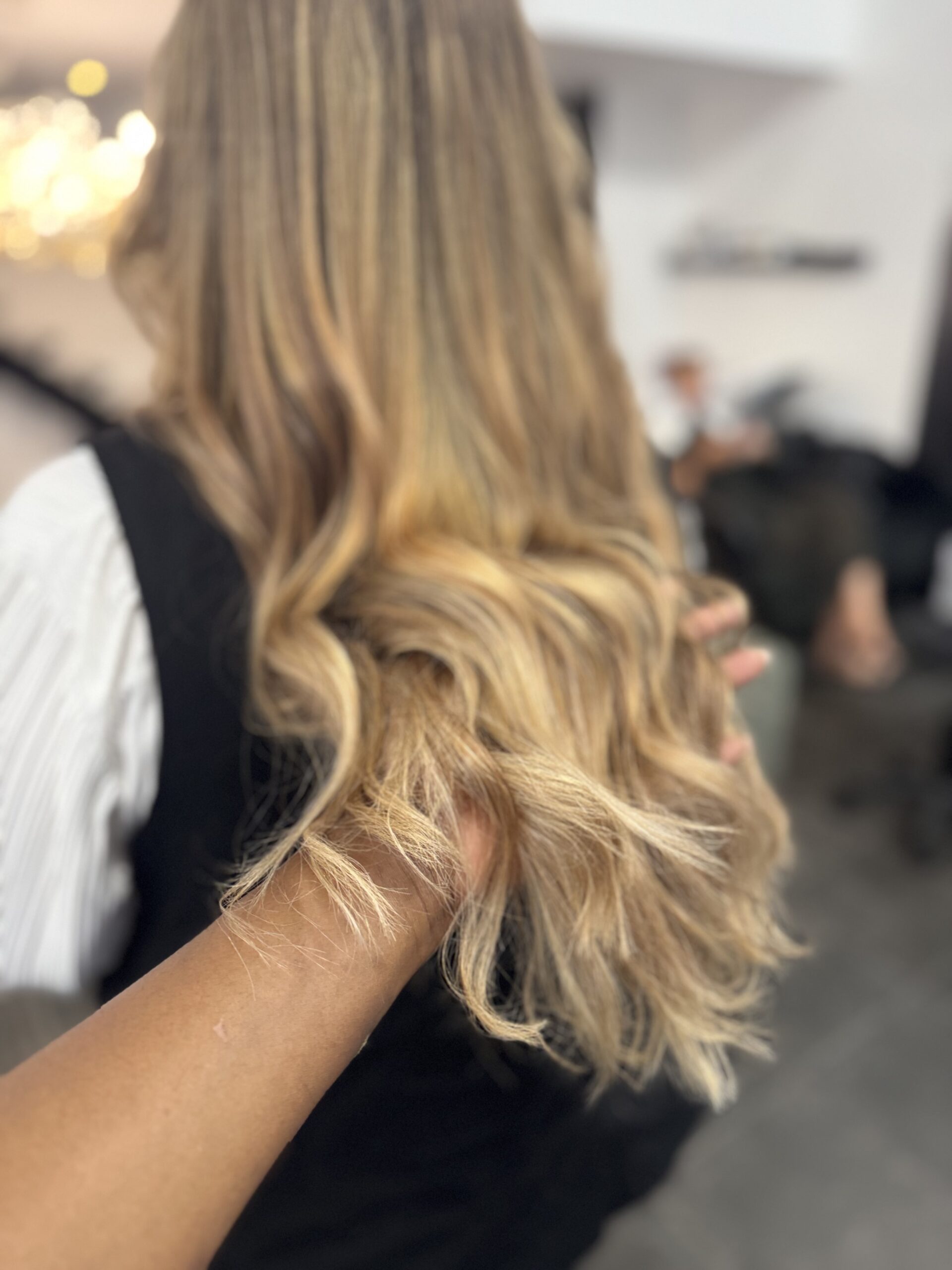 Vue de dos de cheveux mi-longs ondulés aux pointes, balayage blond doré, miel et beige sur base châtain clair