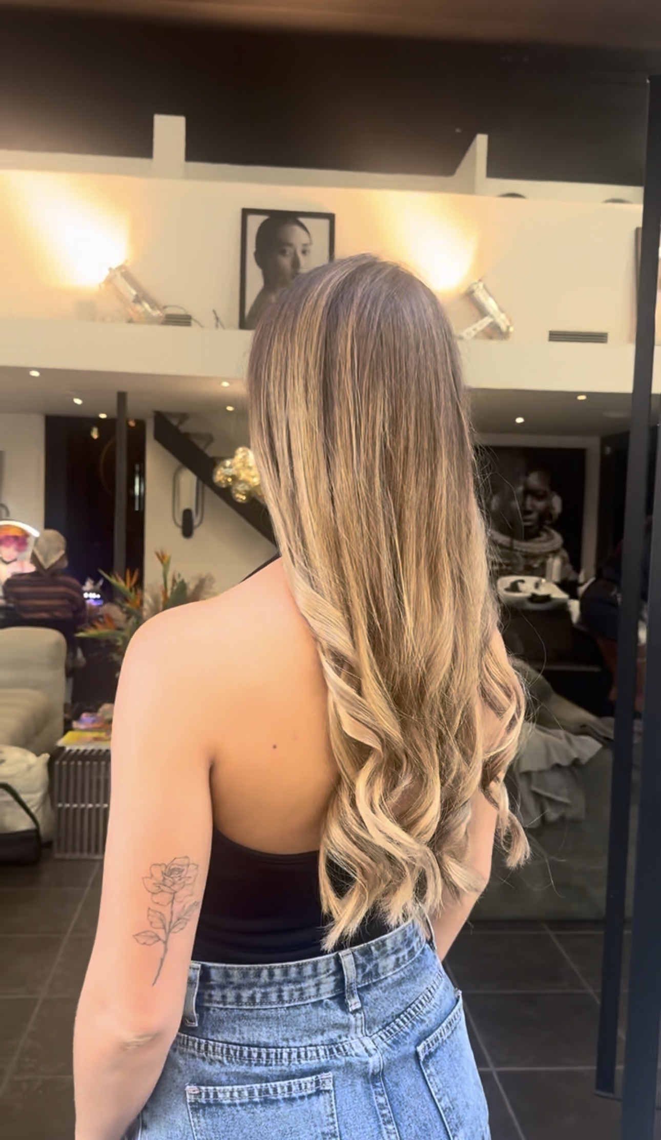 Vue de dos de cheveux longs aux pointes ondulées, balayage blond doré, miel et beige sur base châtain clair