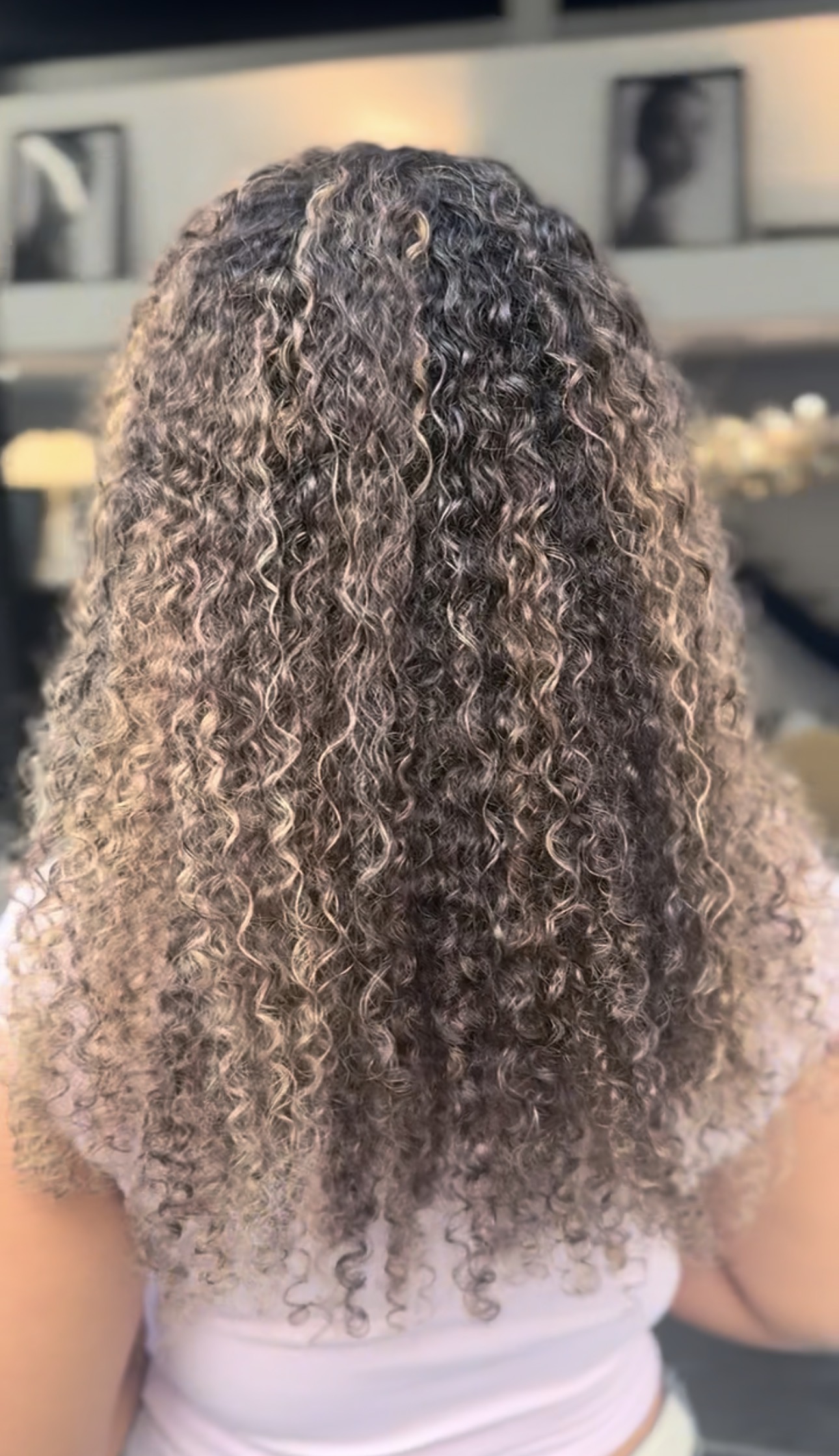 Vue de dos de cheveux mi-longs aux boucles serrées, balayage blond cendré et caramel doré sur base châtain foncé