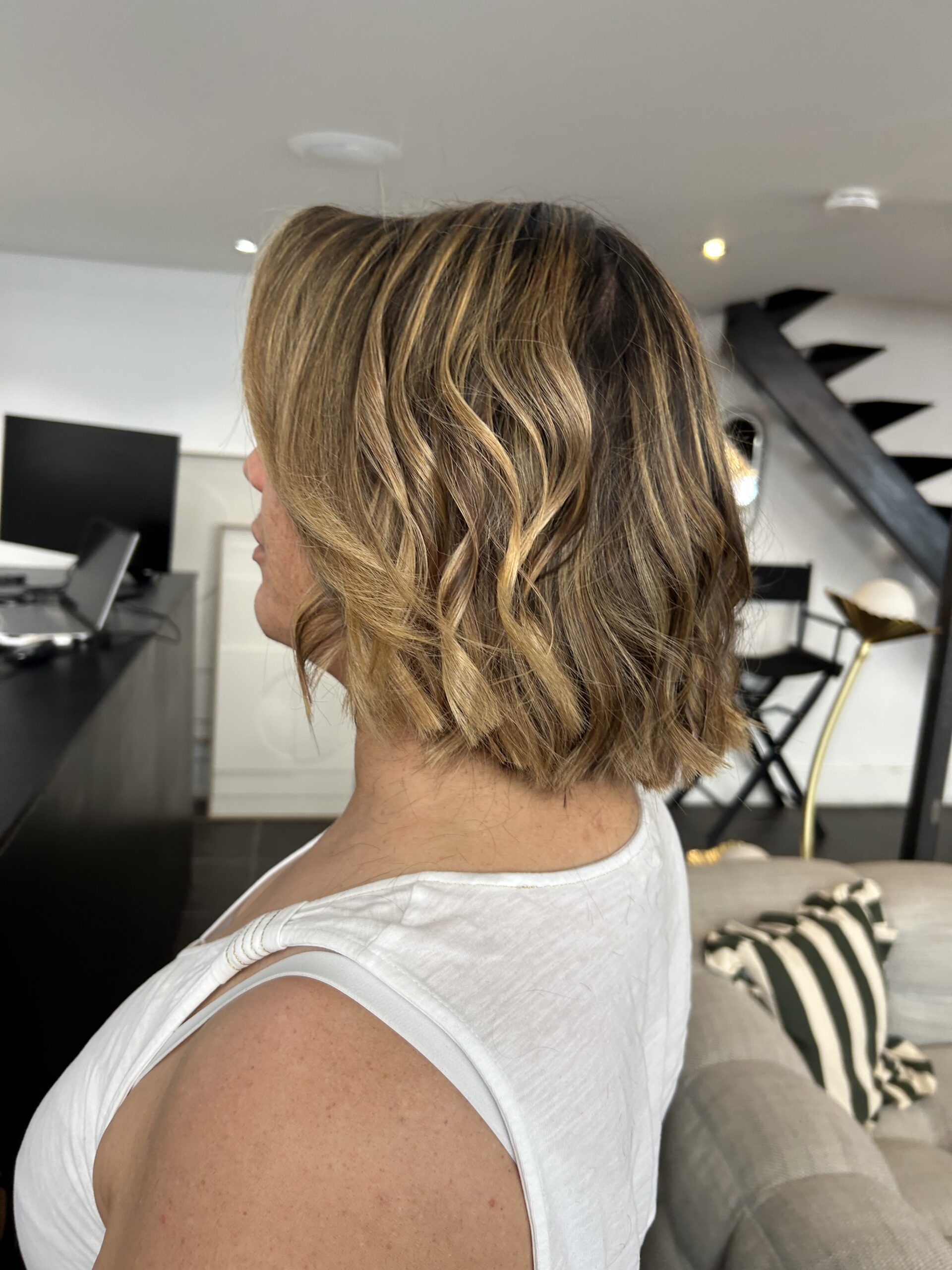 Vue de trois-quarts dos d'un carré court ondulé, mèches châtain clair et blond doré, balayage lumineux