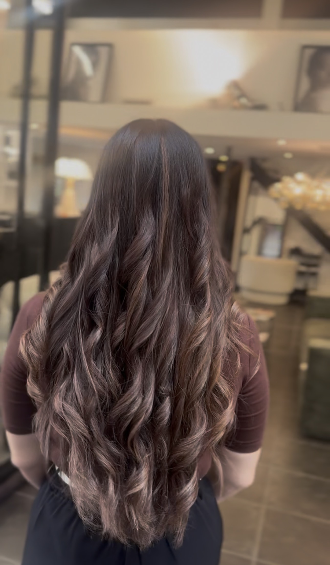 Vue de dos de longs cheveux bruns ondulés, balayage subtil aux reflets noisette et caramel