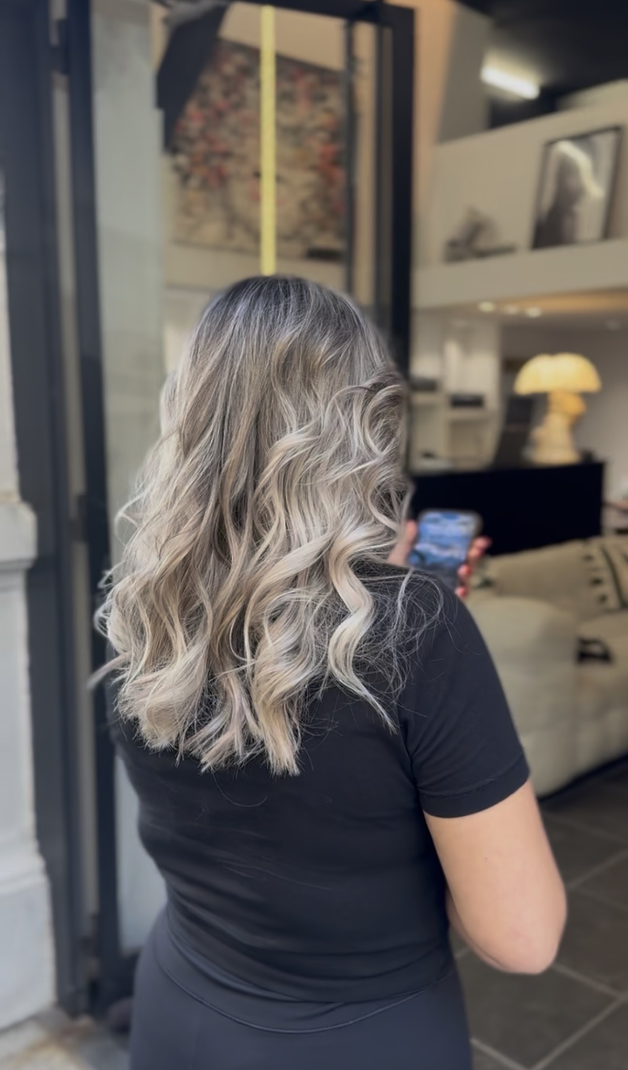 Vue de dos de cheveux mi-longs ondulés, balayage blond polaire et cendré fondu sur base châtain foncé