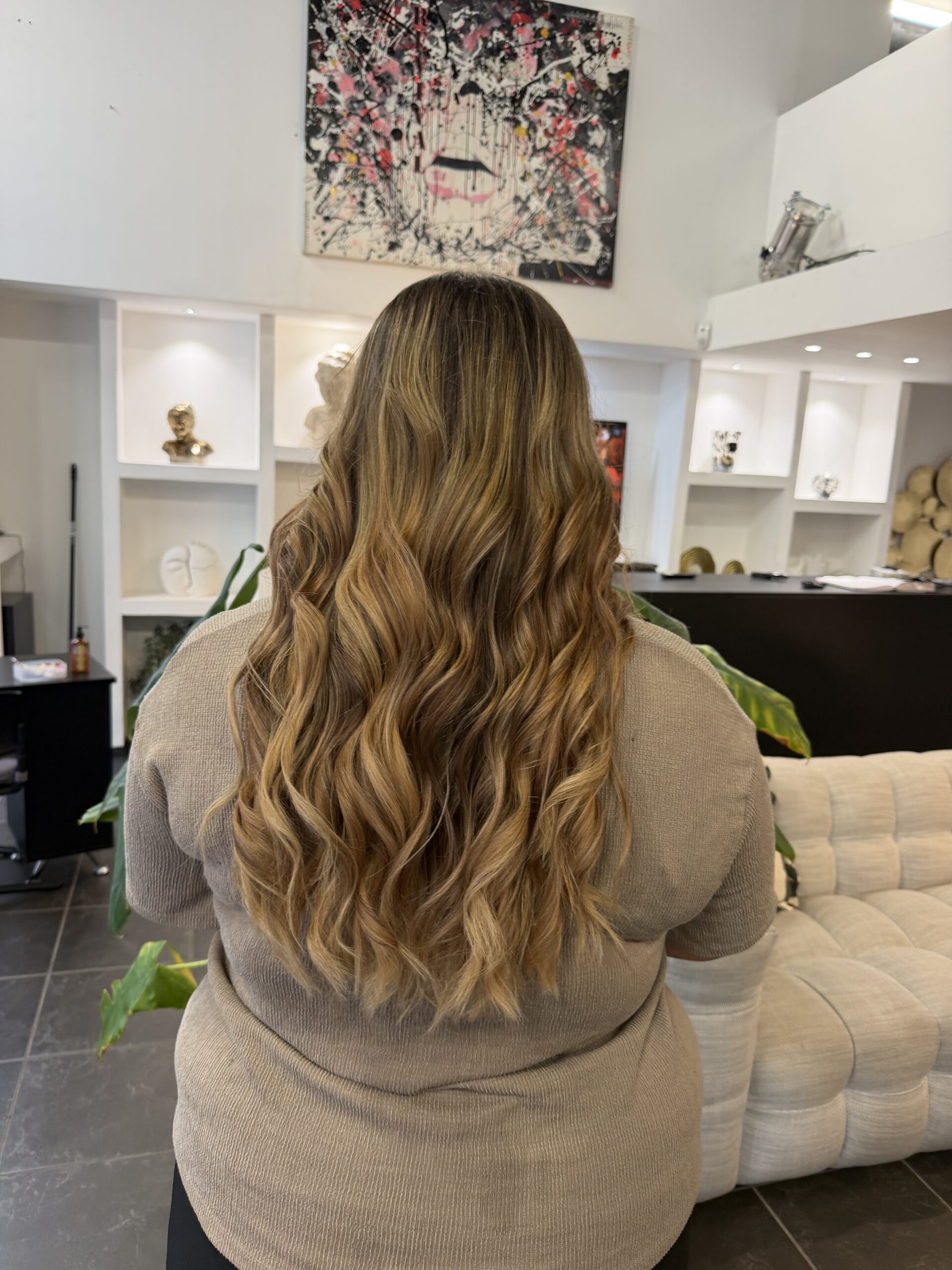 Vue de dos de cheveux longs ondulés, balayage blond miel et caramel sur base châtain clair