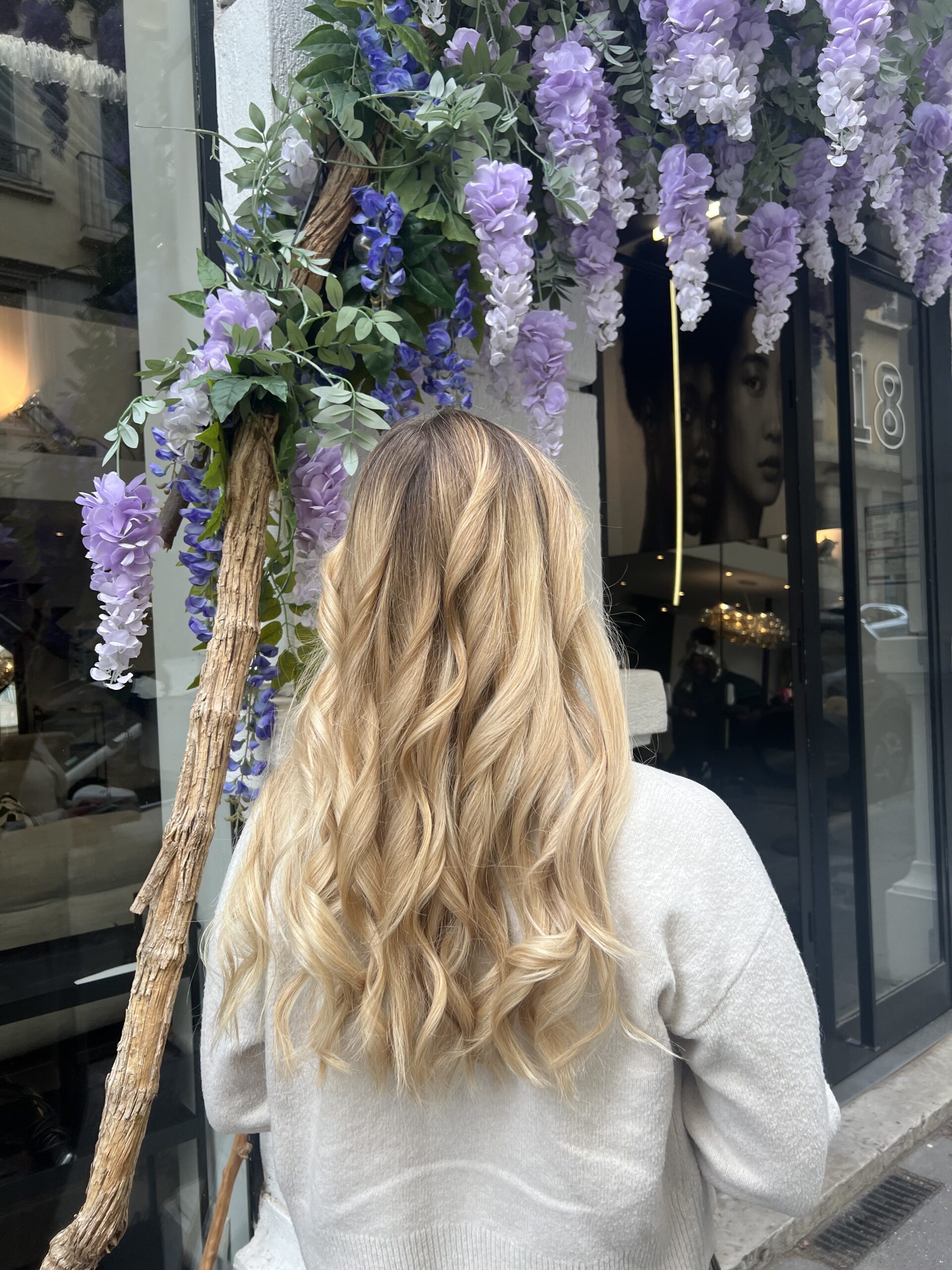 Blond doré miel avec balayage subtil sur cheveux longs ondulés, vu de dos devant le salon