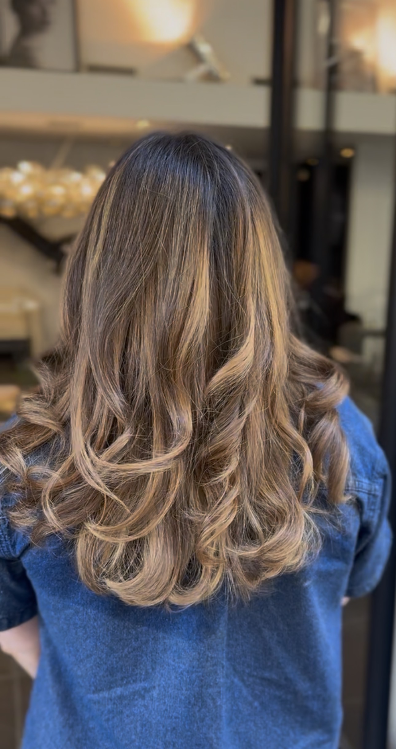 Vue de dos de cheveux mi-longs châtain clair, balayage blond miel et pointes ondulées