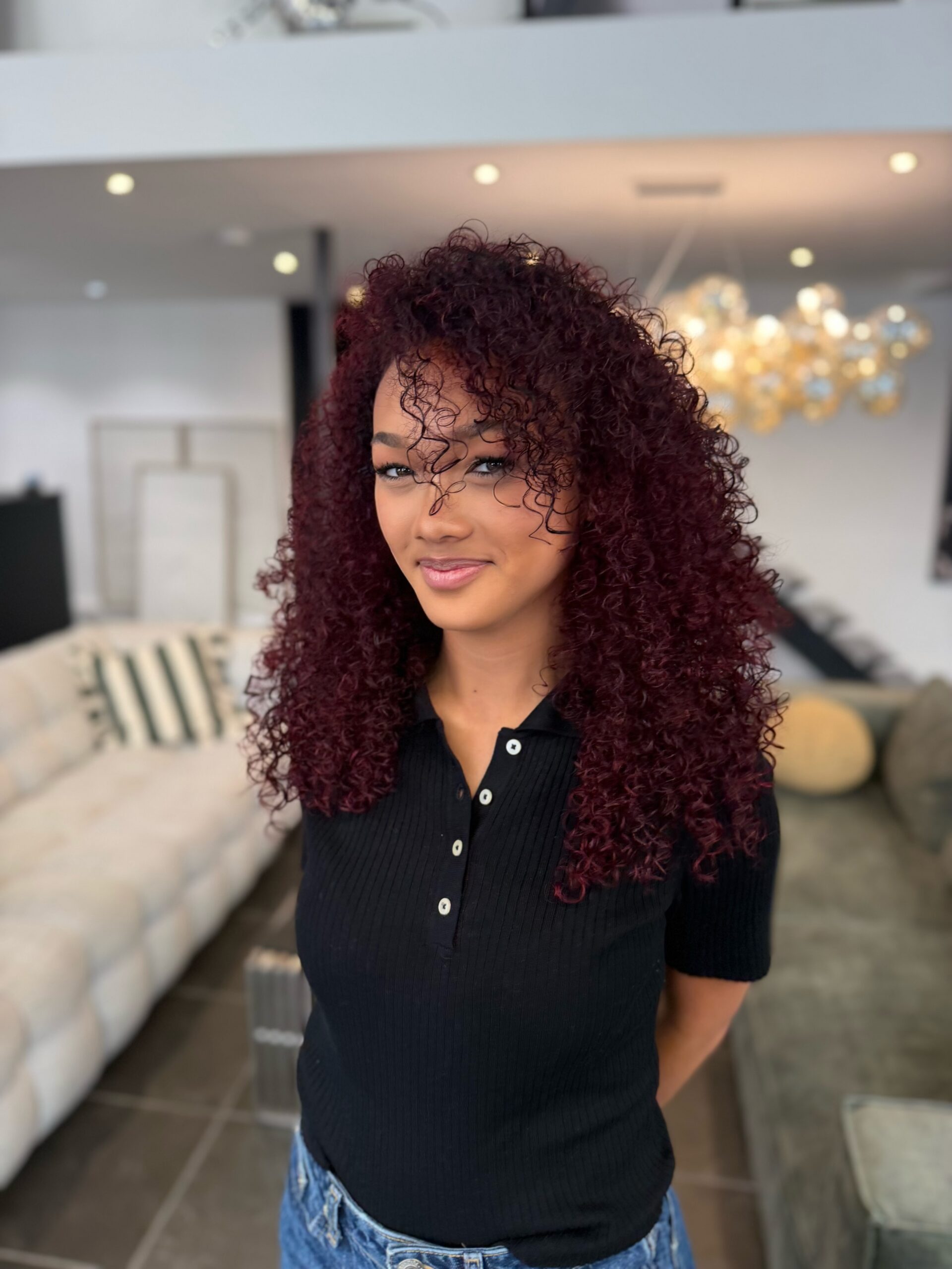 Coloration bordeaux sur cheveux bouclés mi-longs, reflets profonds et volume naturel