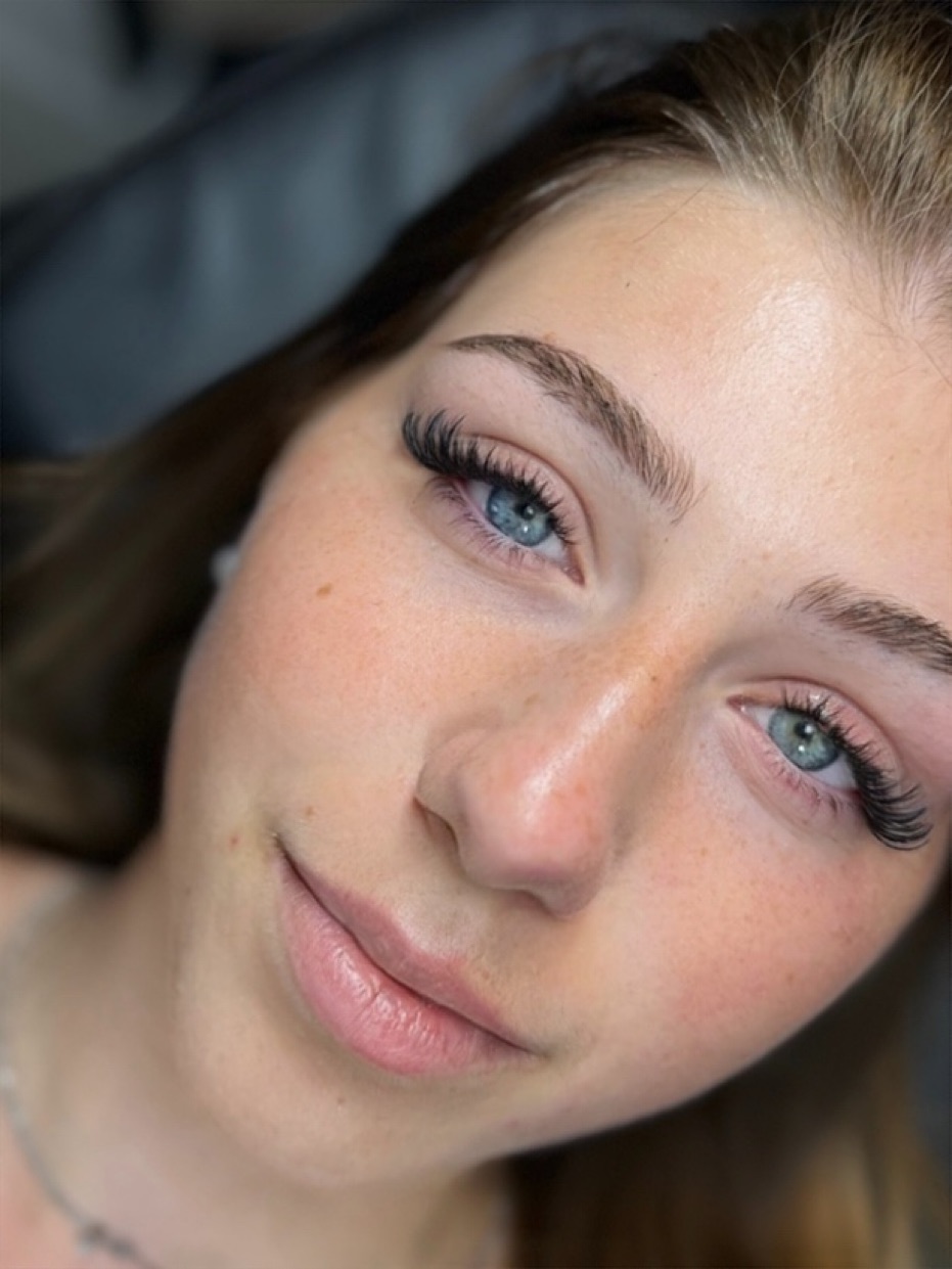 Portrait d'une jeune femme aux yeux clairs, extensions de cils volumineuses et courbées, sourcils naturels